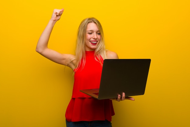 Foto jong meisje met rode kleding over gele muur met laptop en het vieren van een overwinning