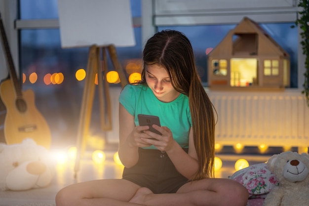 Jong meisje met smartphone zittend in schemerkamer