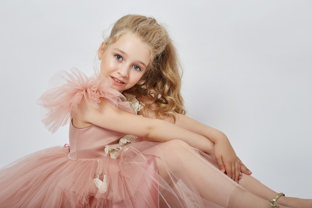 Jong meisje missen schoonheid in een mooie jurk. Cosmetica en make-up voor kinderen. Meisje poseren op een lichte muur. Grappige emoties en verrassing.