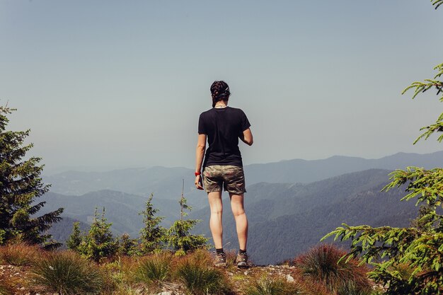 Jong meisje permanent bovenop klif in zomer bergen genieten van uitzicht op de natuur