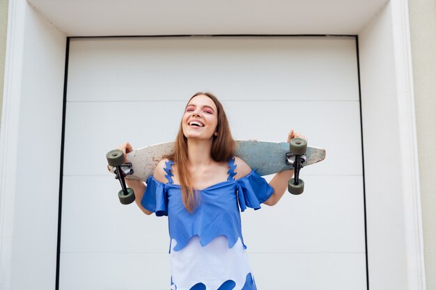 Jong meisje permanent met skateboard buiten lachen over witte muur achtergrond