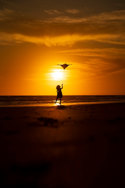 jong meisje spelen met vlieger op het strand bij zonsondergang