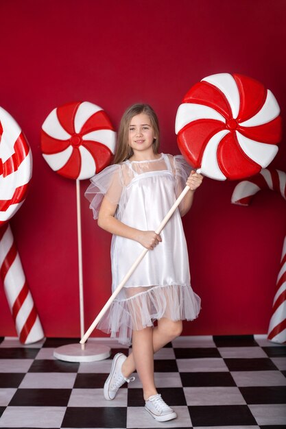 Jong meisje staat met enorme kerstsnoepjes op een rode achtergrond