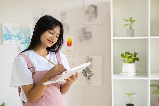 Jong meisje staat op de vloer en houdt kleurenpalet vast en borstel op kamer Hobby en kunststudie thuis