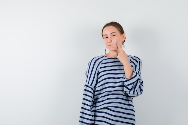 Jong meisje toont haar puffende wangen met haar vinger op witte achtergrond