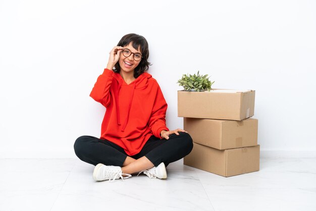 Jong meisje verhuizen in nieuw huis tussen dozen geïsoleerd op een witte achtergrond met een bril en happy