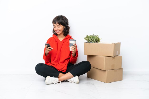Jong meisje verhuizen in nieuw huis tussen dozen geïsoleerd op een witte achtergrond met koffie om mee te nemen en een mobiel