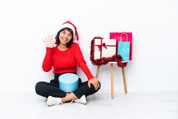 Jong meisje viert Kerstmis zittend op de vloer geïsoleerd op een witte bakcground tellen vijf met vingers