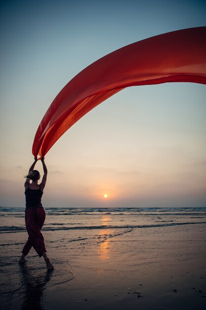 jong meisje voert dansbewegingen op het zand met een lange rode doek