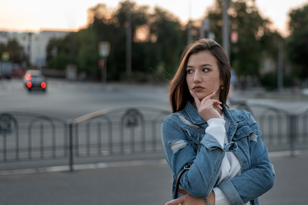 Jong meisje wacht op iemand langs de weg. Portret van student op stadsoppervlak. Avondwandeling.