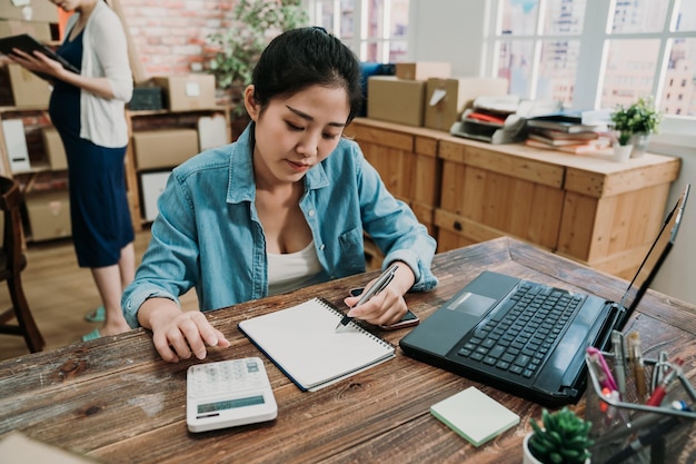 jong meisje werknemer hand met pen schrijven notitie over boek zit aan bureau. online marketing verpakkingsdoos en levering MKB-concept. zwangere vrouw manager bedrijfseigenaar die achteraan staat te werken op tablet