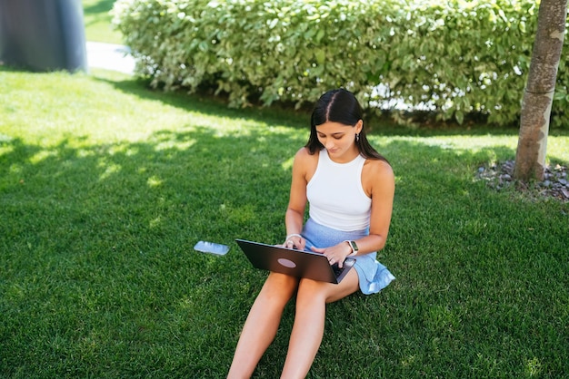 Jong meisje werkt met een laptop zittend op het gazon