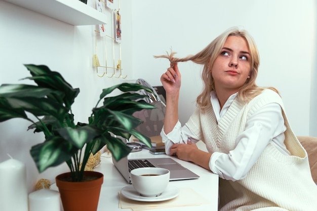 Jong meisje windt haar haar op een vinger met een peinzend gezicht aan een werktafel