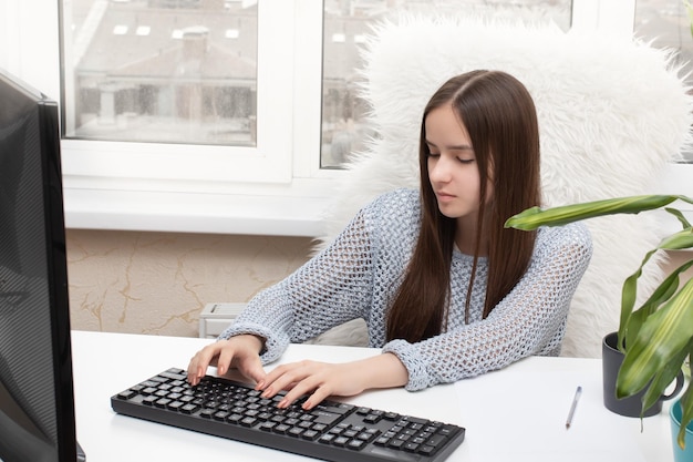 Jong meisje zit aan een tafel te typen op een computer glimlachend