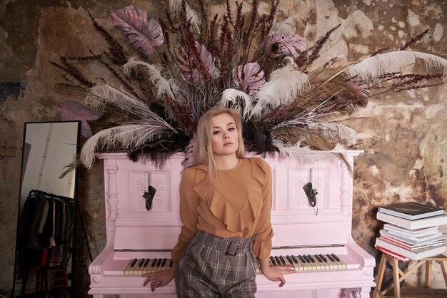 jong meisje zit op een roze piano. Schoonheid portret van een blonde in korte broek een oude bakstenen muur