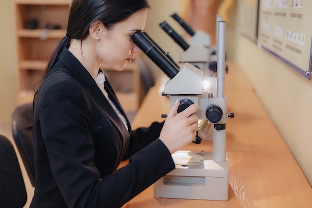 Jong meisje zitten aan de tafel en werken met een microscoop