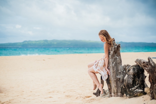 Jong meisje, zittend op een oude boom op het strand van Boracay