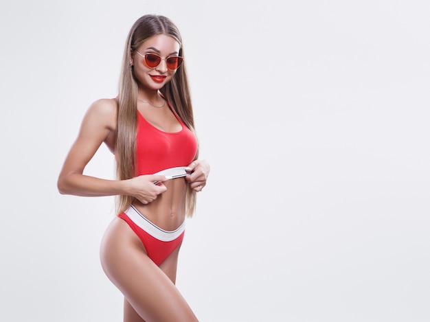 Jong model met een perfect lichaam in rode lingerie en zonnebril op een witte achtergrond