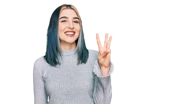 Jong modern meisje met casual trui die laat zien en omhoog wijst met vingers nummer drie terwijl ze zelfverzekerd en gelukkig glimlacht.
