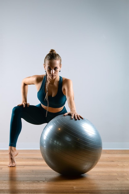 Jong mooi atletisch meisje doet oefeningen op fitball in de sportschool op een grijze achtergrond sporten