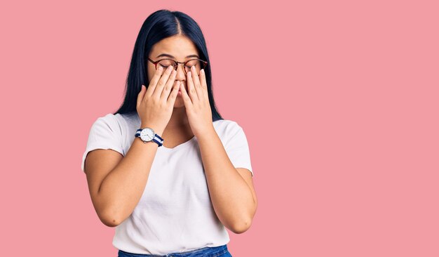 Jong mooi Aziatisch meisje dat vrijetijdskleding en een bril draagt en ogen wrijft voor vermoeidheid en hoofdpijn, slaperig en vermoeid gezichtsprobleem met expressie
