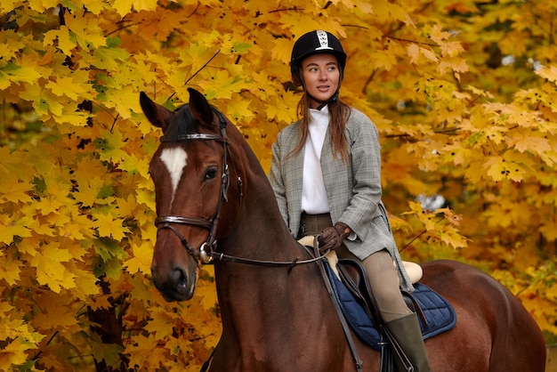 Jong mooi donkerbruin meisje berijdt een paard op een warme en zonnige herfstdag Portret van een mooie jonge vrouw op het paard die lange laarzen en handschoenen draagt