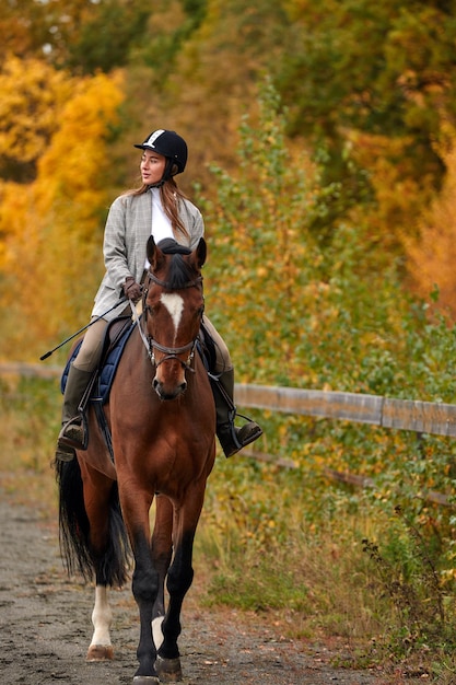 Jong mooi donkerbruin meisje berijdt een paard op een warme en zonnige herfstdag portret van een mooie jonge vrouw op het paard die lange laarzen en handschoenen draagt