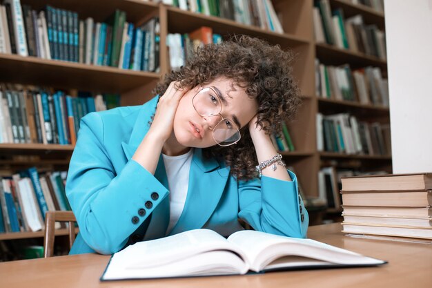 Jong mooi krullend meisje dat in glazen in bibliotheek zit