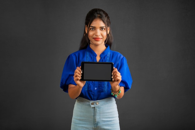 Jong mooi meisje dat een leeg scherm van een smartphone of mobiel of tablettelefoon op een grijze achtergrond toont