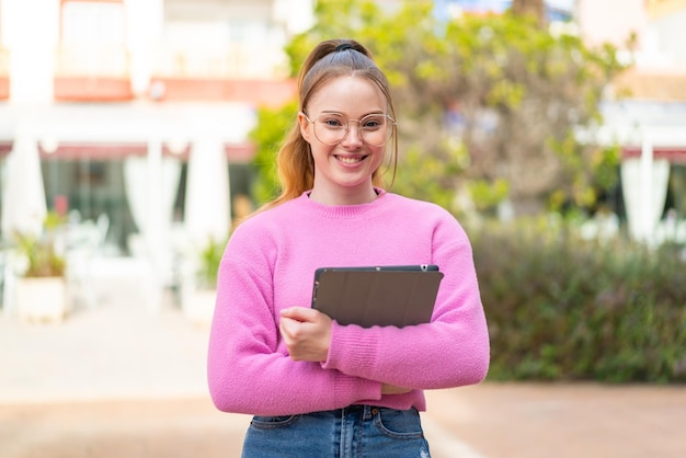 Jong mooi meisje dat in openlucht een tablet met gelukkige uitdrukking houdt