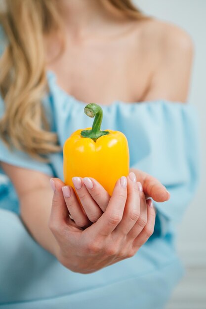 Foto jong mooi meisje dat verse gele peper op witte achtergrond houdt. het concept van gezond eten. tonen.