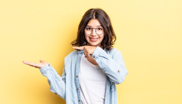 Jong mooi meisje dat vrolijk lacht en wijst naar de ruimte op de palm aan de zijkant te kopiëren, een object laat zien of er reclame voor maakt