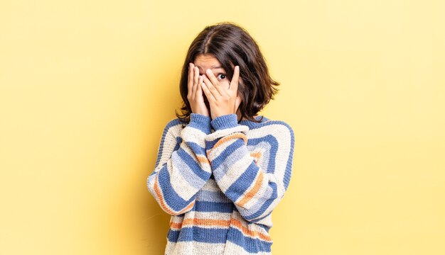 jong mooi meisje dat zich bang of beschaamd voelt, gluurt of spioneert met ogen half bedekt met handen