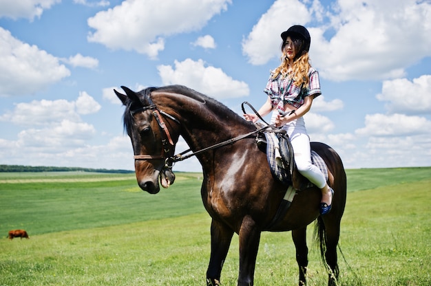 Jong mooi meisje die een paard berijden op een gebied bij zonnige dag.