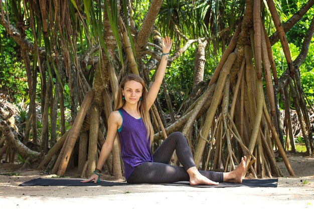 Jong mooi meisje doet yoga onder de palmbomen