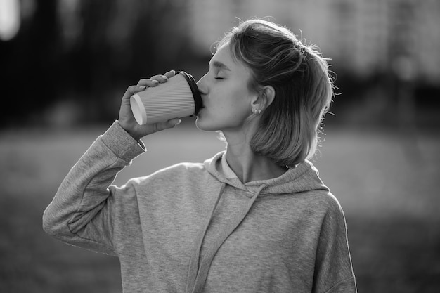 Jong mooi meisje drinkt lat uit een papieren beker op straat zwart-wit foto
