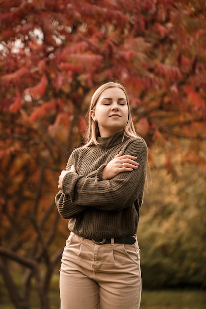 Jong mooi meisje gekleed in stijlvolle kleding, groene trui en beige broek, in een herfstpark met prachtige bomen