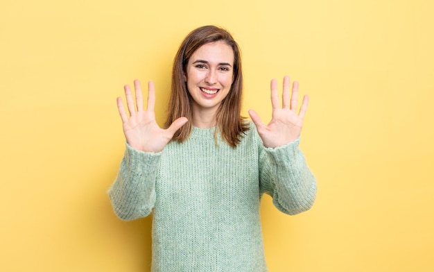 Jong mooi meisje glimlachend en vriendelijk kijkend, nummer tien of tiende met hand naar voren tonend, aftellend