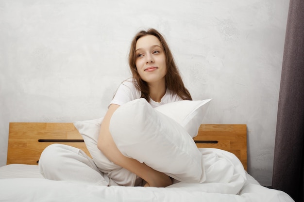 Jong mooi meisje glimlachend zittend in bed en kussen knuffelen