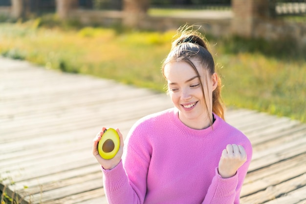 Jong mooi meisje houdt een avocado buiten om een overwinning te vieren