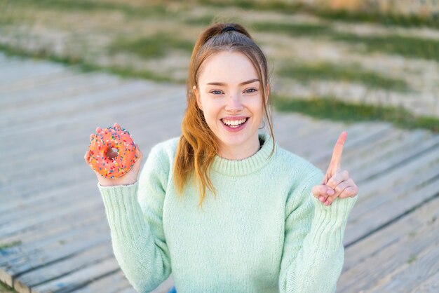 Jong mooi meisje houdt een donut buitenshuis en wijst op een geweldig idee