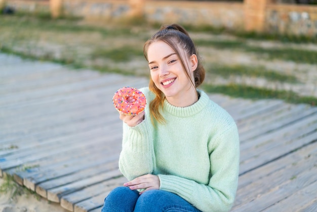 Jong mooi meisje houdt een donut in de open lucht met een gelukkige uitdrukking