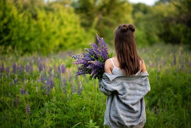 Jong mooi meisje houdt in haar handen lente-lupinebloemen en keerde haar selectieve focus terug