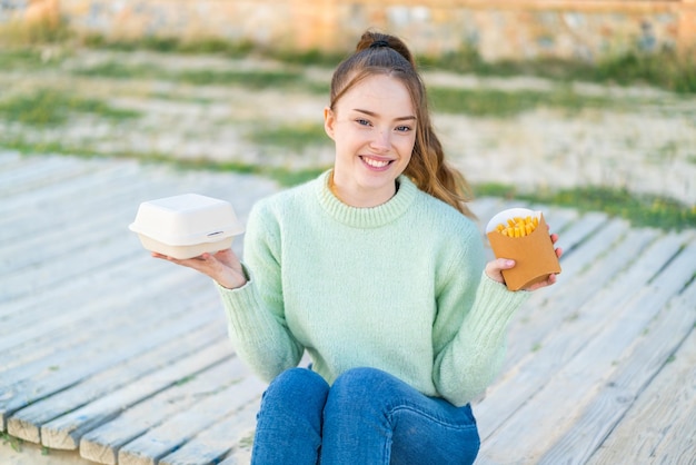 Jong mooi meisje in de buitenlucht met gebakken frites en afhaalmaaltijden met een gelukkige uitdrukking