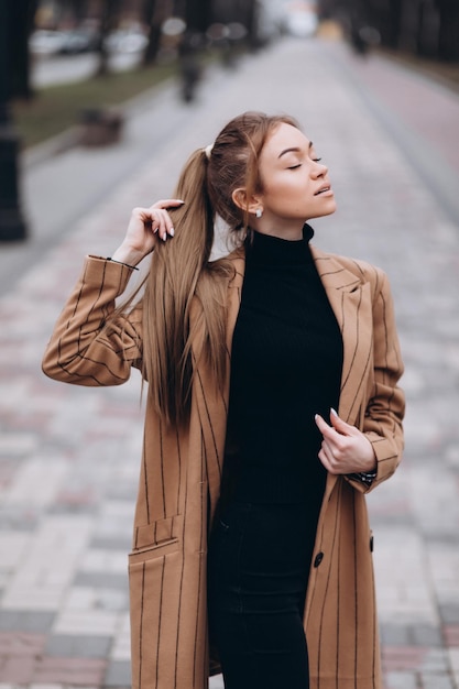 Jong mooi meisje in een beige jas poseren in de straten van de stad. kleding advertentie