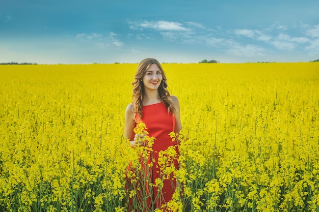 Jong mooi meisje in een rode jurk close-up in het midden van het gele veld met de radijs bloemen. Lente seizoen
