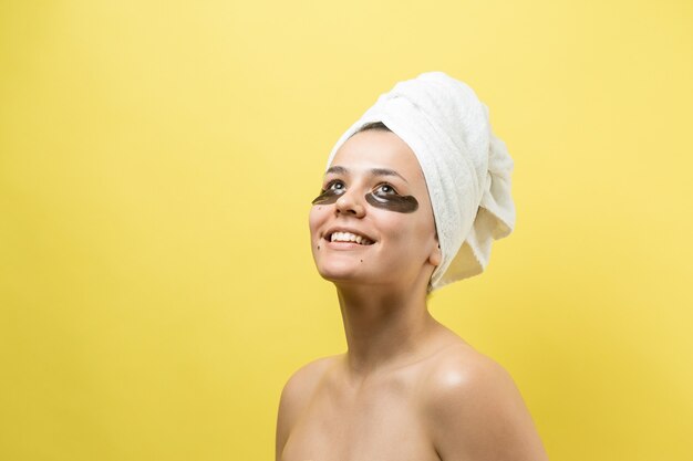 Jong mooi meisje in een witte handdoek op zijn hoofd draagt collageengelpleisters onder haar ogen. Masker onder ogen behandeling gezicht.