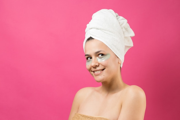 Jong mooi meisje in een witte handdoek op zijn hoofd draagt collageengelpleisters onder haar ogen