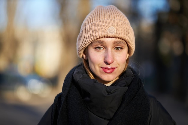 jong mooi meisje in een zwart donsjack en bruine hoed op een onscherpe achtergrond op straat