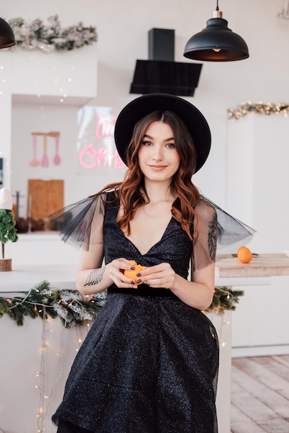 Jong mooi meisje in een zwarte jurk en een hoed maakt een mandarijn schoon